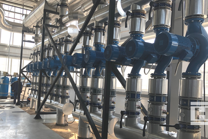 Row of industrial blue water pumps and stainless steel pipes inside Project Norby greenhouse heating system.