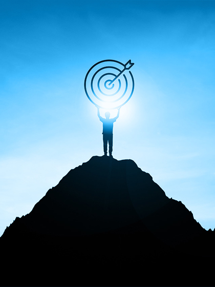 Silhouette of a person standing on a mountain peak, holding a target symbol with an arrow, representing entrepreneurship and goal achievement.