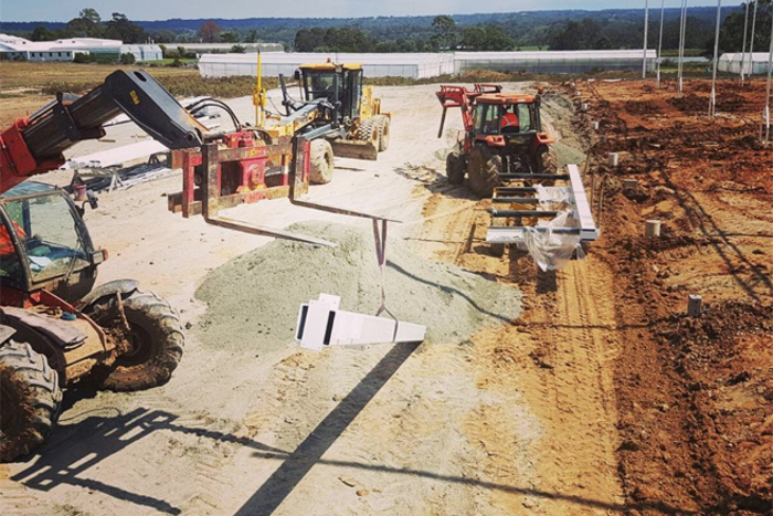Greenhouse construction site with heavy machinery and tractors working on foundation and steel structures