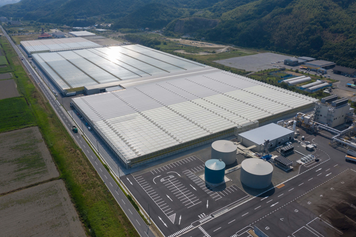 Aerial view of a large turnkey greenhouse complex in Kasaoka, Japan, featuring glass-covered structures, water tanks, and modern climate control facilities.