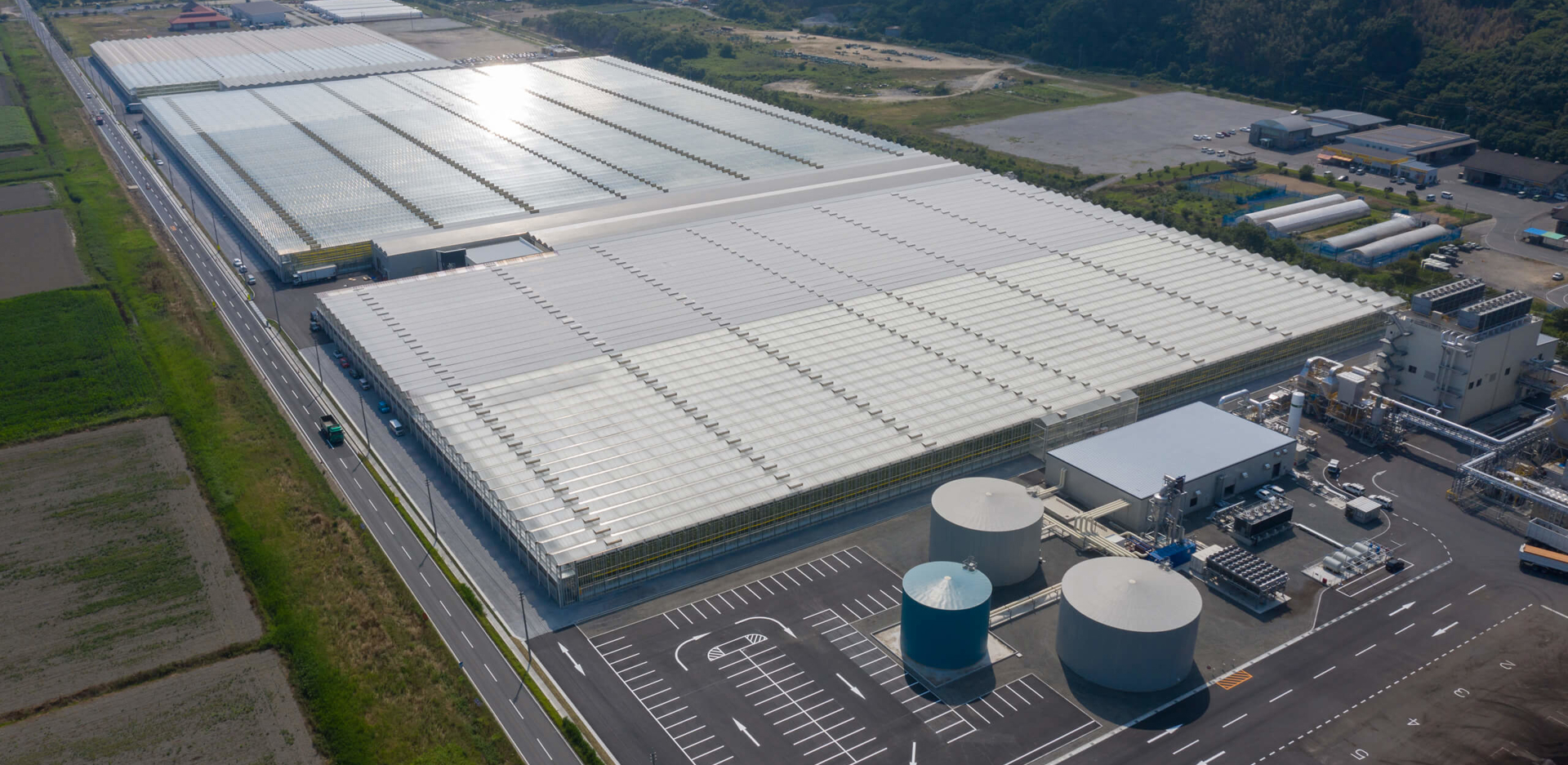 Aerial view of a large turnkey greenhouse complex in Kasaoka, Japan, featuring glass-covered structures, water tanks, and modern climate control facilities.