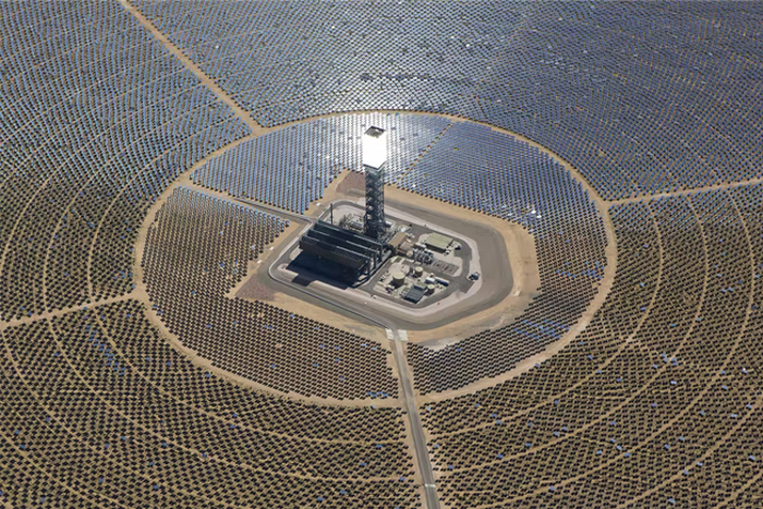 Aerial view of a large solar power plant with a central tower, surrounded by hundreds of mirrored panels concentrating sunlight to generate renewable energy.
