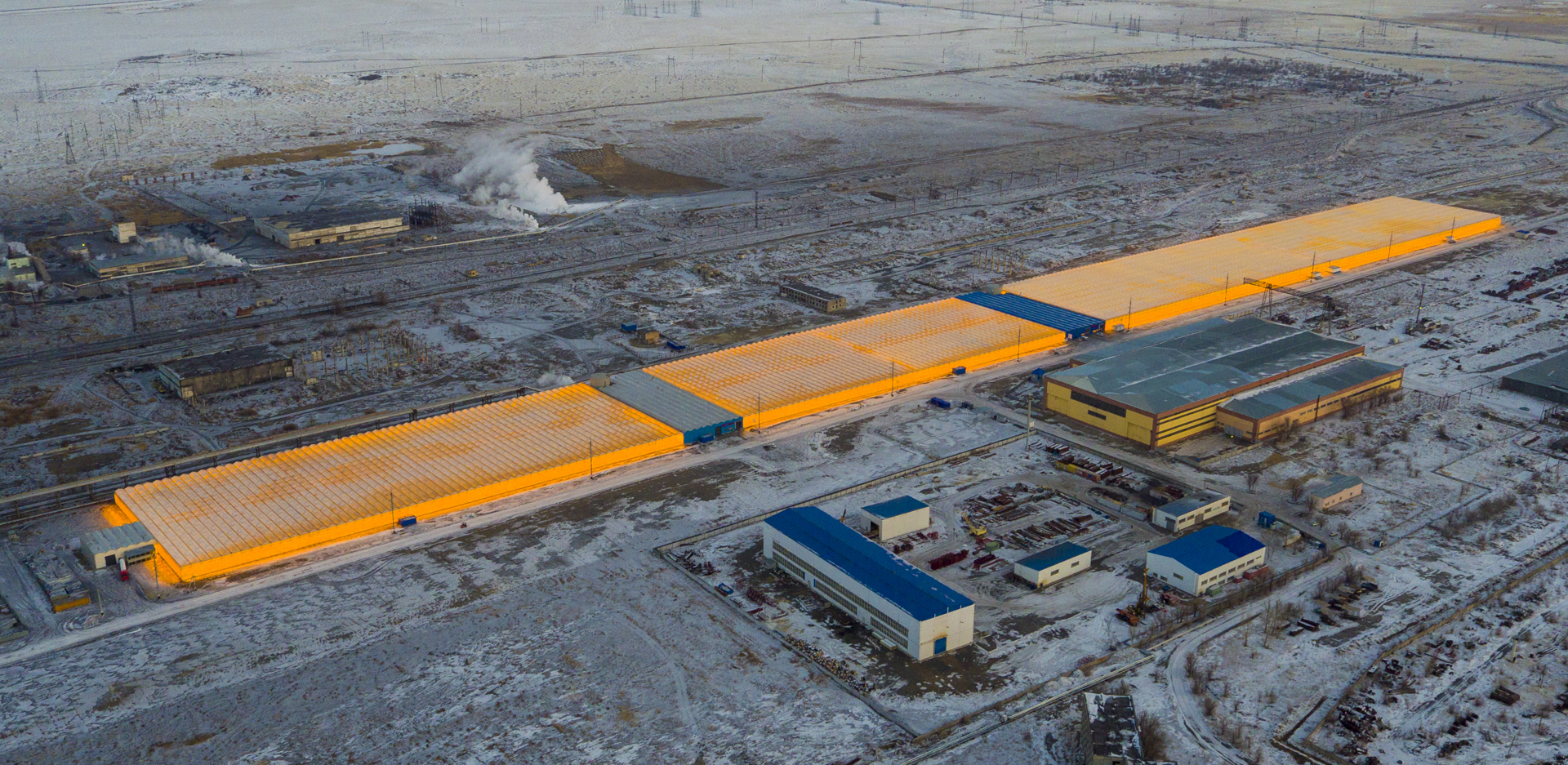 Aerial view of the Van Der Hoeven KAZ Ekibastuz II greenhouse complex glowing orange in the snowy Kazakh landscape.