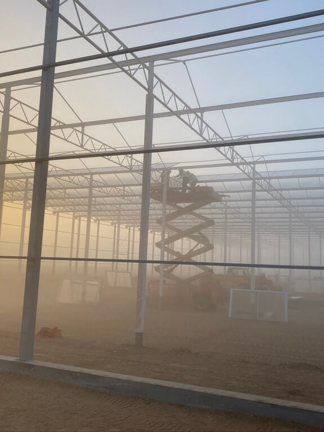 Greenhouse construction at Armela with workers during sunset.